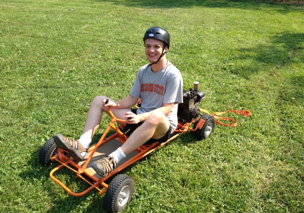 A man sitting in a go cart on the grass in the sunshine.